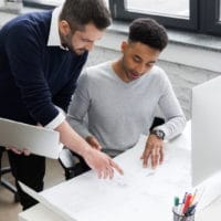 two-smiling-male-office-workers-working-with-lapto-PRX35BX